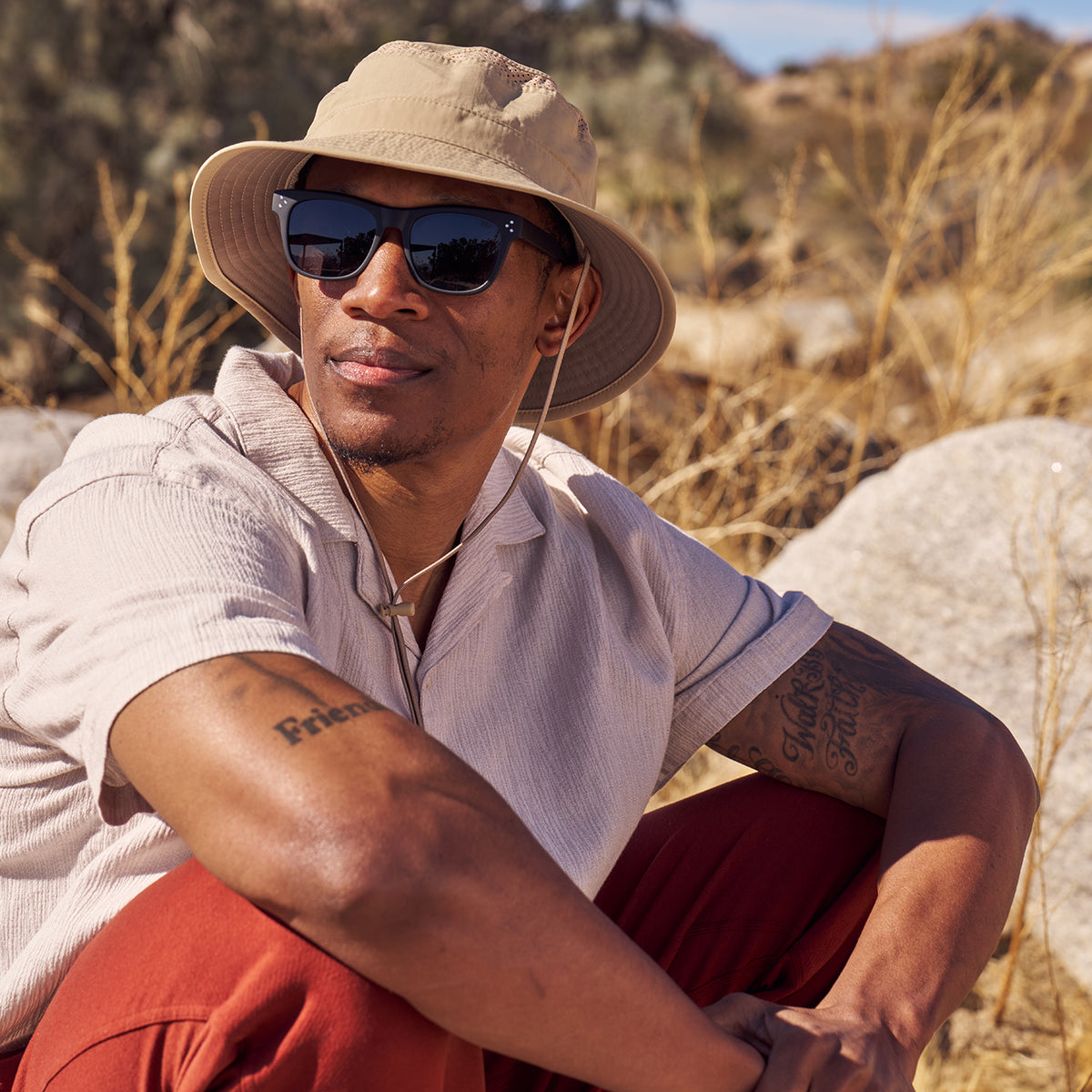 A man sitting in a desert setting wearing a Sunday Afternoons Solar Bucket Hat